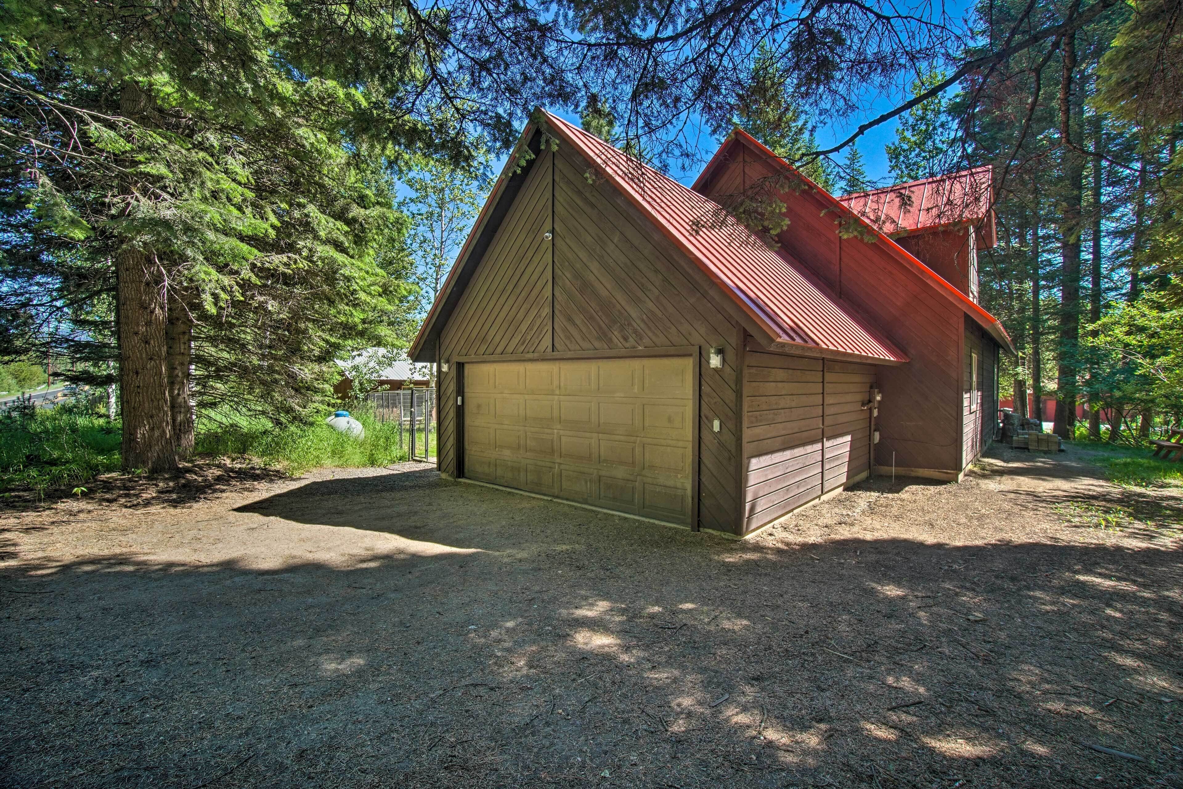 En træhytte med rødt tag, en garage og omgivet af tæt skov.