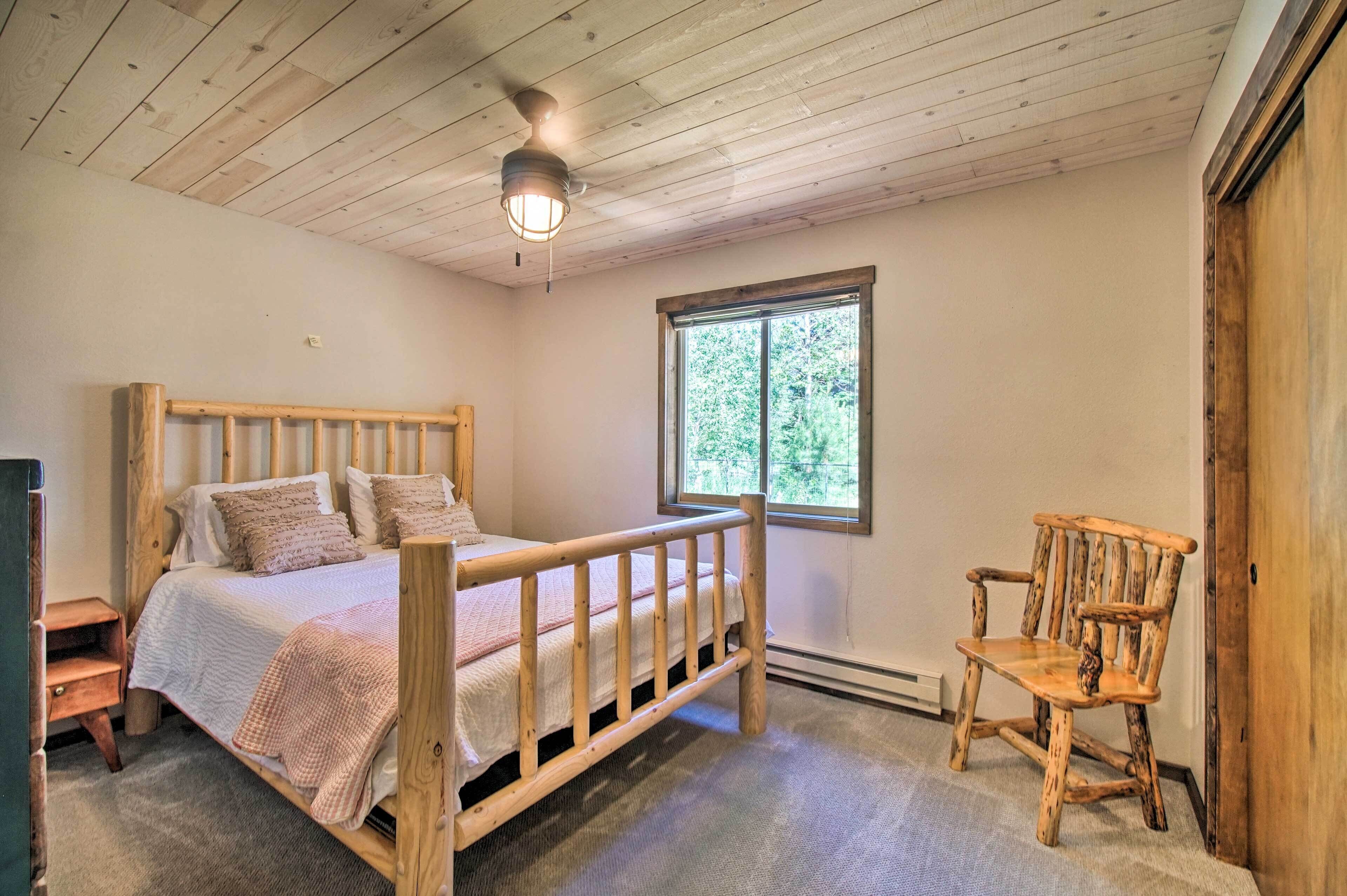 Ein Bett mit Holzkopfteil, ein kleiner Holzstuhl und ein Fenster mit Blick auf Bäume.
