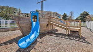 A playground with a blue slide, wooden play structures, and a wooden bridge. - Bright Manistee Condo w/ Beach + Pool Access! (Manistee)