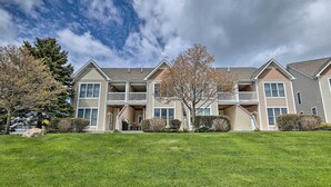 A multi-story residential building with a front porch, a covered outdoor seating area, and a well-maintained lawn. - Bright Manistee Condo w/ Beach + Pool Access! (Manistee)