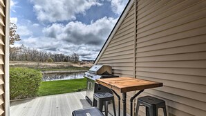 An outdoor patio with a grill, a wooden table, and two stools. - Bright Manistee Condo w/ Beach + Pool Access! (Manistee)