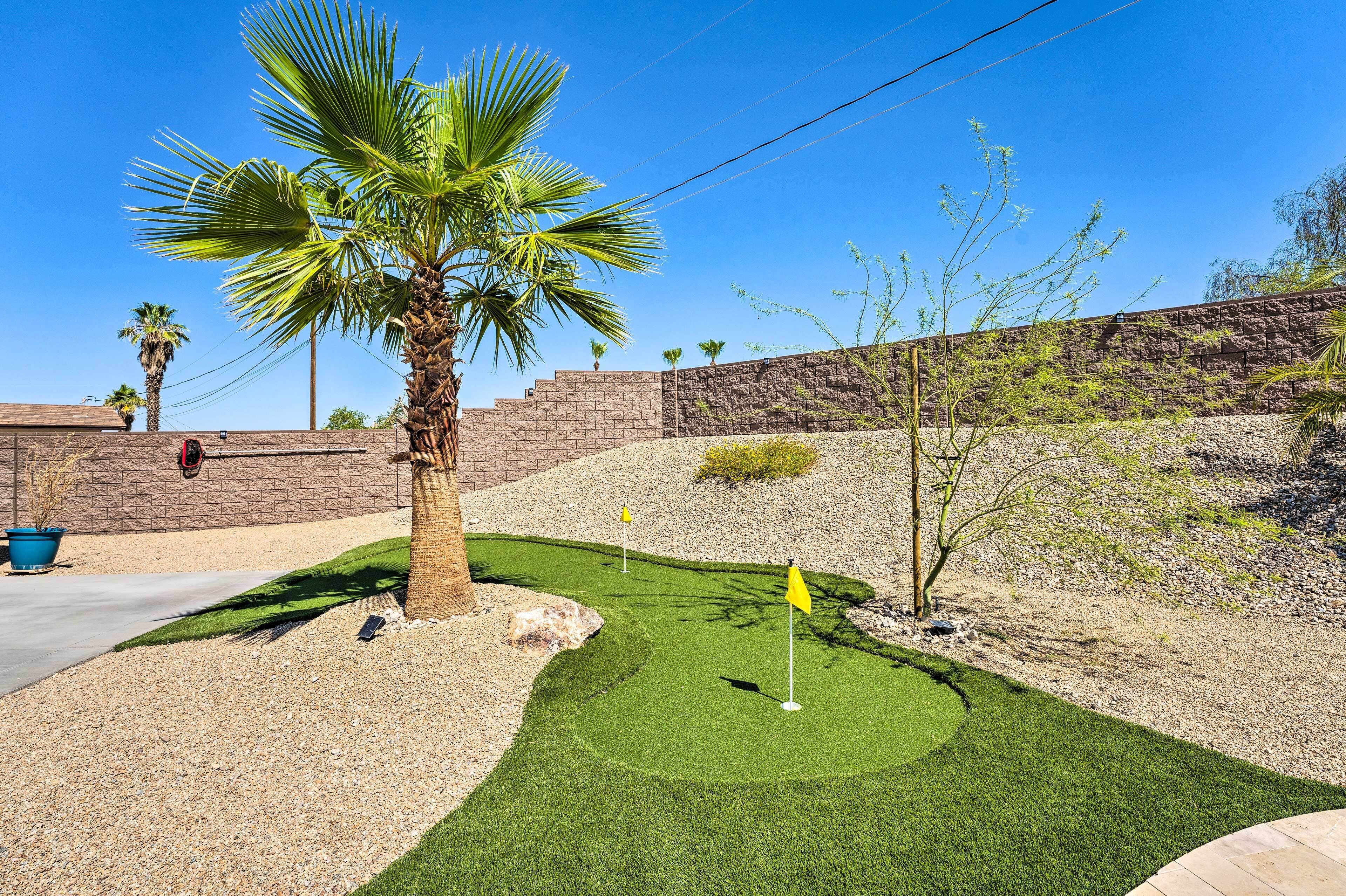 Un campo de golf bien cuidado con un sendero despejado, palmeras y un muro de piedra al fondo.