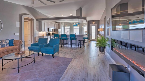 A spacious living area with a modern ceiling fan, a kitchen in the background, and a large TV mounted on the wall. - 4 Mi to Lake Havasu State Park: Home w/ Pool (Lake Havasu City)