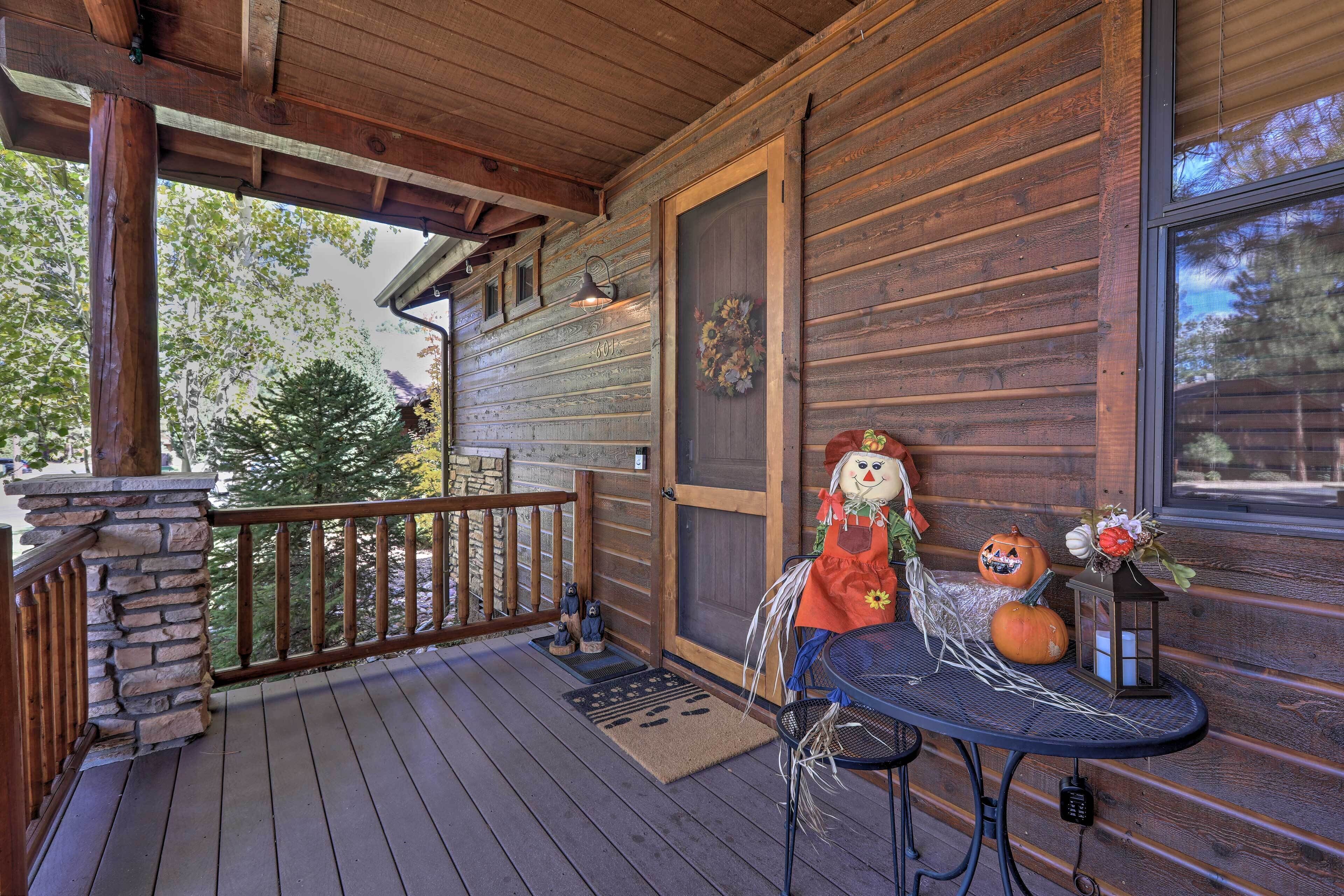 A wooden porch with a stone pillar, a small table with Halloween decorations, and a door with a wreath.