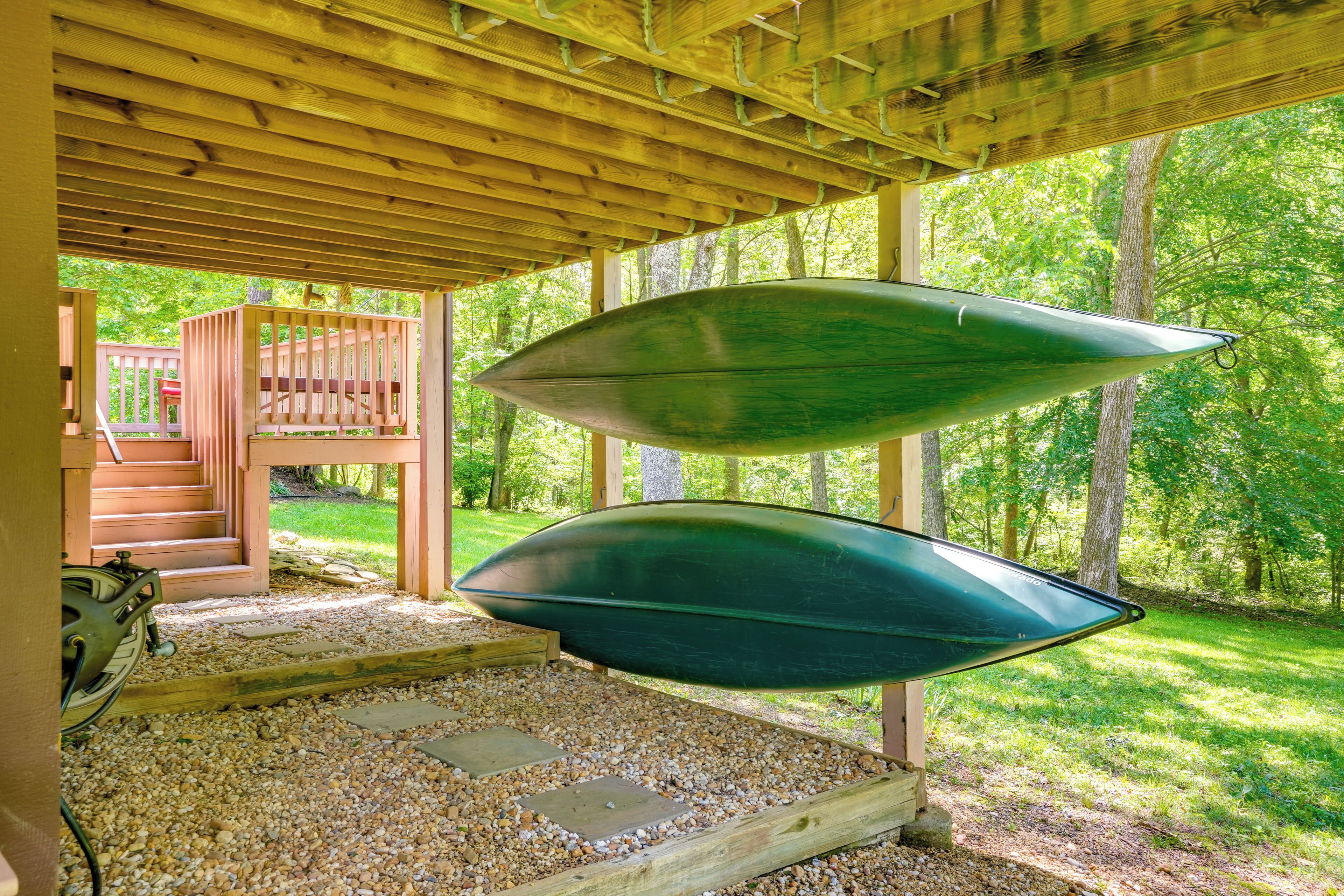A covered wooden structure with two green kayaks hanging from the ceiling, a wooden staircase, and a gravel ground.