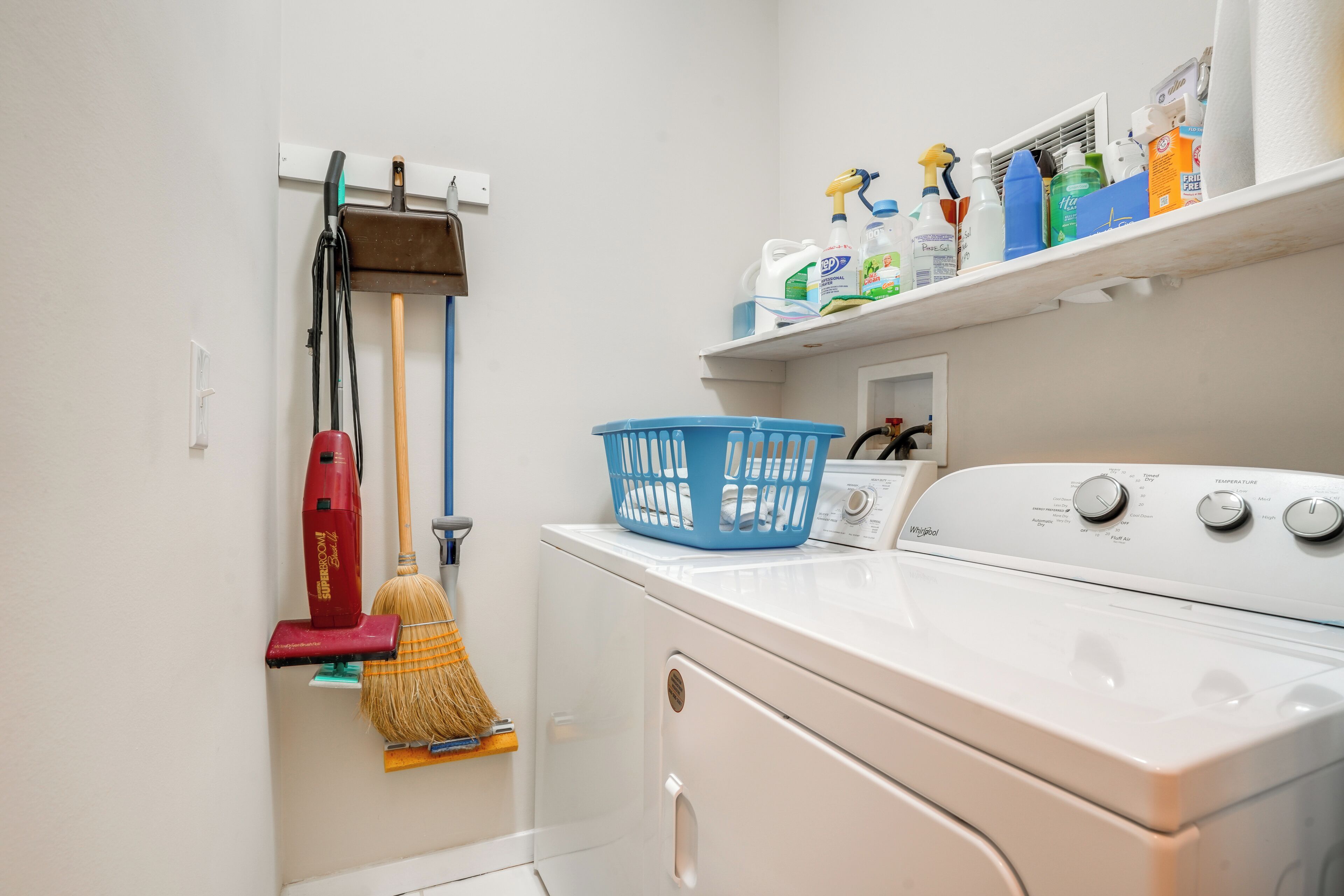 A laundry area with a washing machine, a mop, a broom, and a laundry basket.
