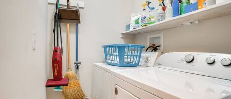 A laundry area with a washing machine, a mop, a broom, and a laundry basket.