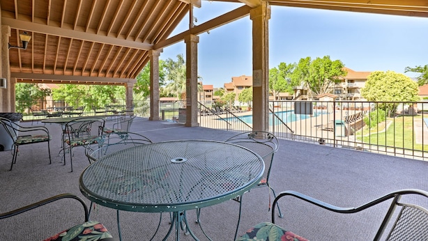 A covered outdoor patio with metal tables and chairs, a pool in the background, and a view of surrounding buildings. - 5 Mi to Town Square Park: Condo in Sports Village (St. George)