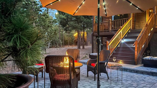 Un patio al aire libre con mobiliario de mimbre, un paraguas grande y una escalera que lleva a un nivel superior.