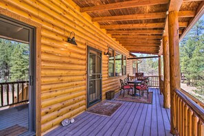 Una baita di legno con un portico coperto, un tavolo da pranzo con sedie e vista sulla foresta circostante.