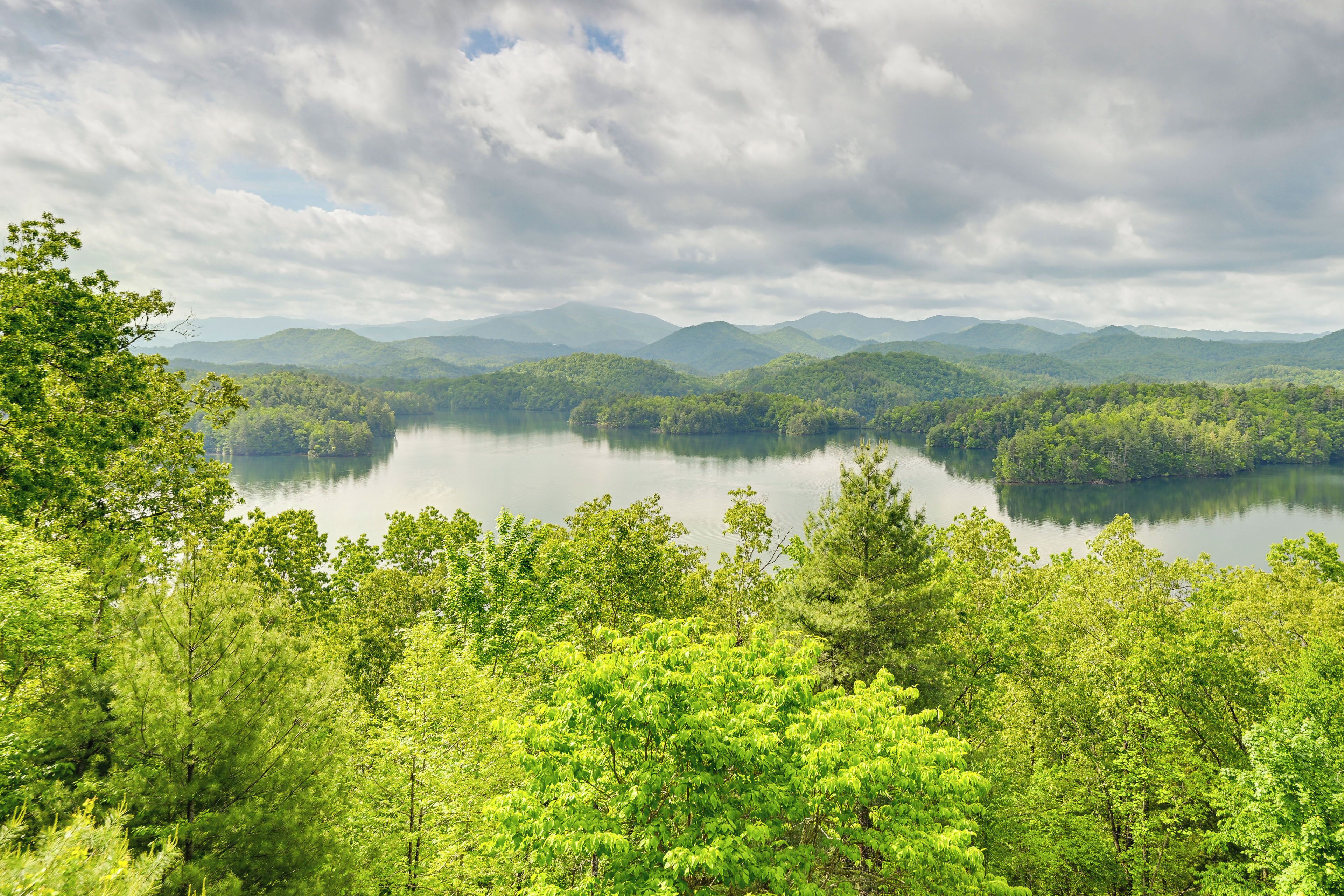 A lake surrounded by dense forest and mountains under a cloudy sky.