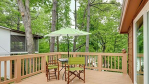 Une terrasse en bois avec une table et des chaises, un parasol à rayures et une vue sur les arbres.
