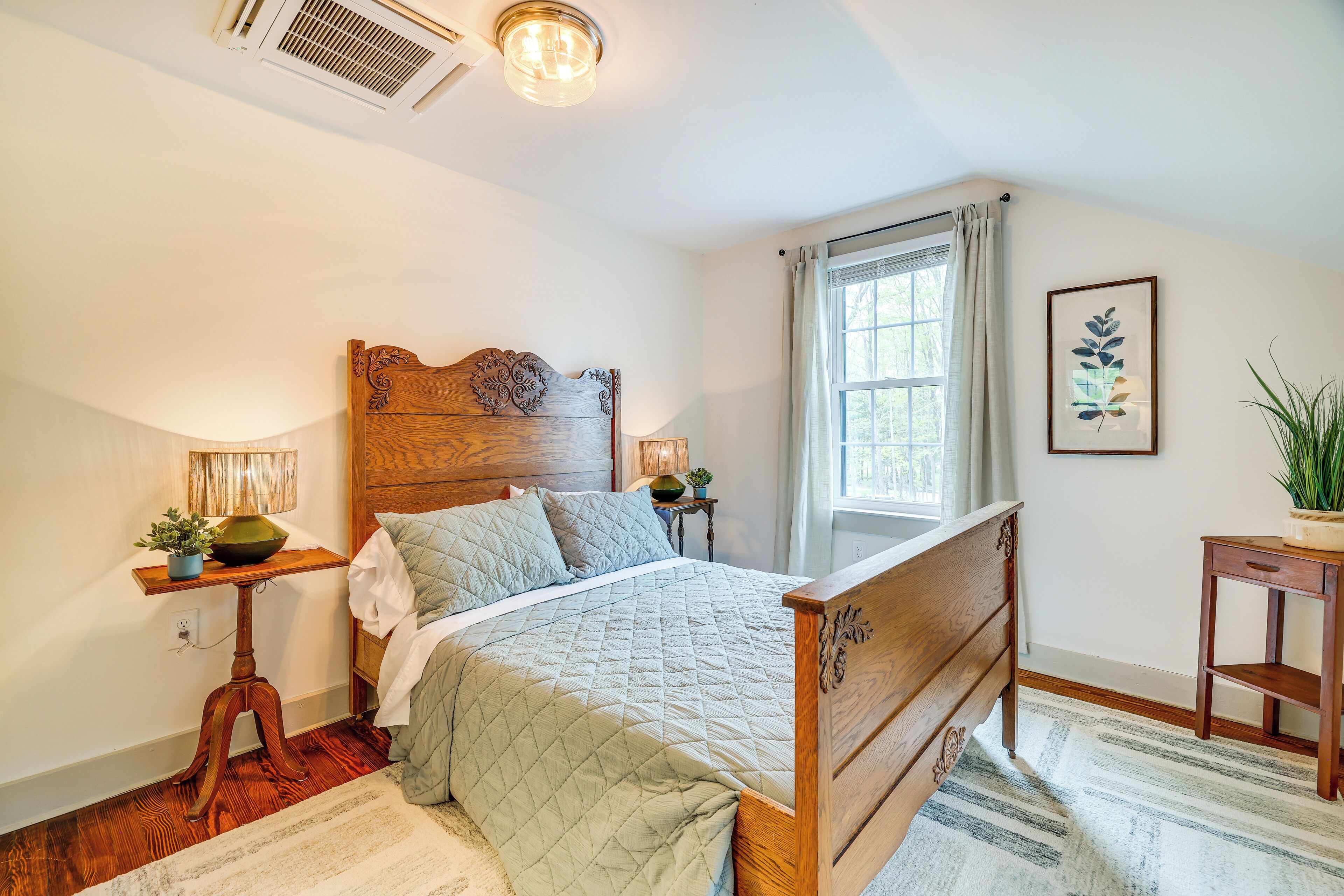 Quarto com cama de madeira, mesa de cabeceira com luminária, janela com cortinas e um quadro na parede.