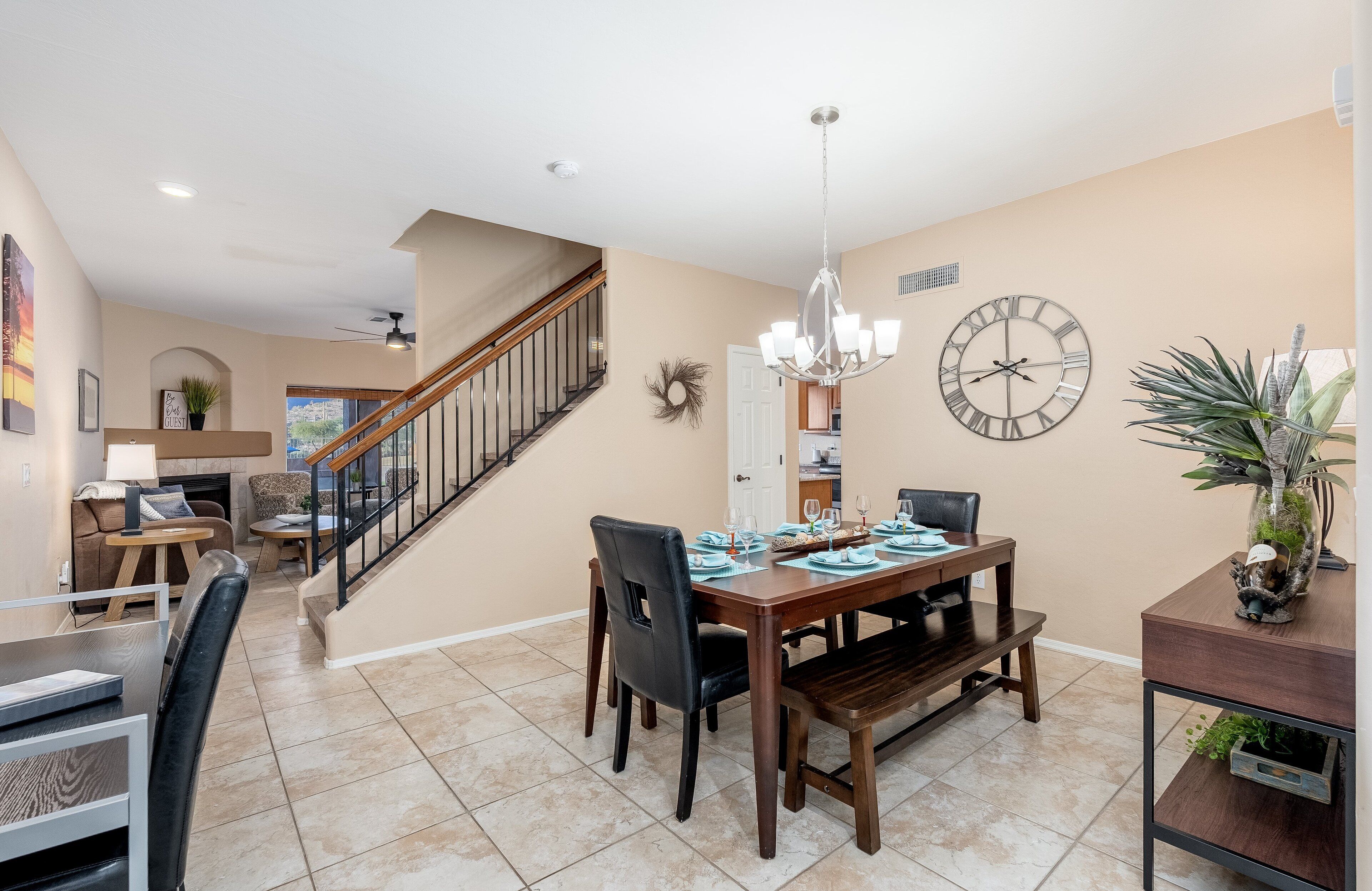 A dining area with a wooden table, chairs, and a chandelier. There is a staircase leading to another room.