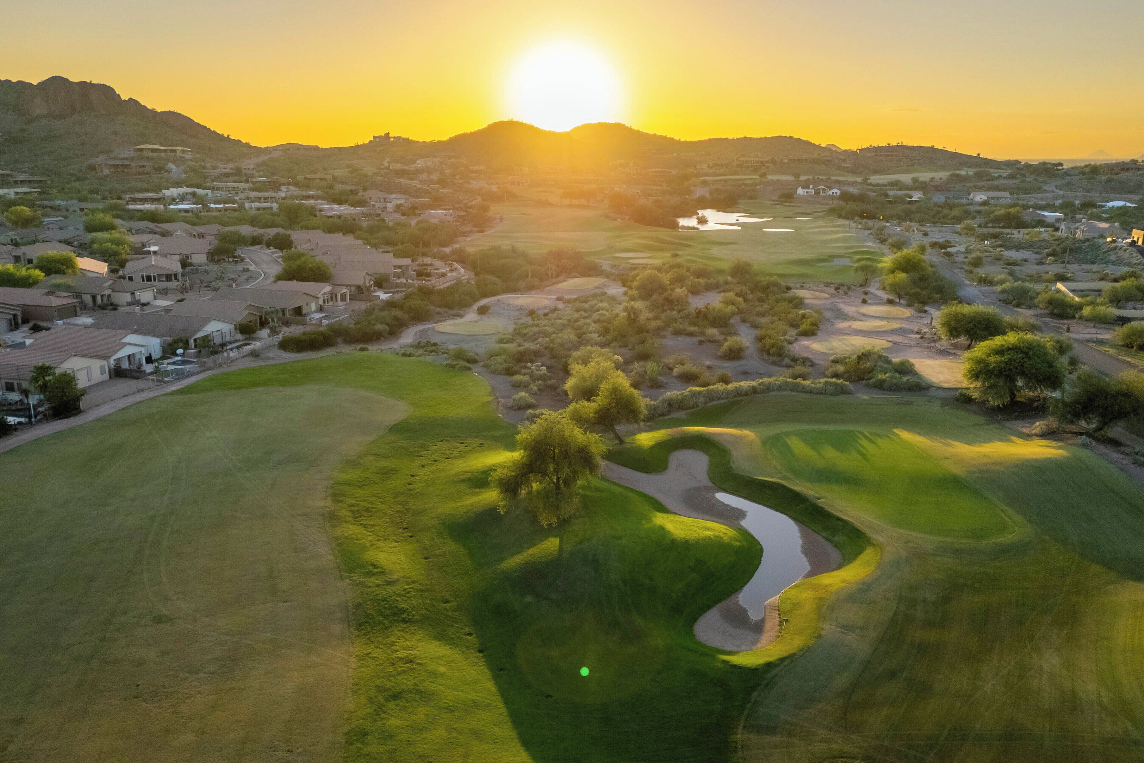 Un terrain de golf avec un coucher de soleil en arri ère-plan, entouré de quartiers résidentiels.
