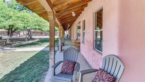 A covered porch with two chairs and a table, a pink building, and a tree in the background. - Arizona Desert Vacation Rental w/ Pool Access! (Eloy)