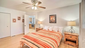 A bedroom with a bed, wooden nightstands, a ceiling fan, and a door leading to a kitchen. - 'the Crooked Pot Cabin' Near Hiking + Dining! (Pine)