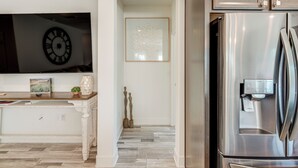 Una cocina moderna con un refrigerador de acero inoxidable, un televisor de pantalla plana montado sobre una encimera de madera y un reloj en la pared.