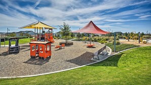 Un parque infantil con diversas estructuras de juego, incluyendo un andamio rojo y columpios amarillos, rodeado de un césped cuidado.