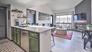 A modern kitchen with a central island, green cabinets, and a large window overlooking a scenic view.