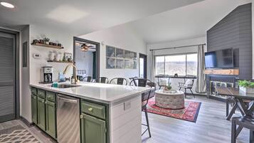 A modern kitchen with a central island, green cabinets, and a large window overlooking a scenic view.