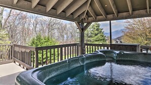A hot tub under a wooden pergola with a view of trees and mountains.