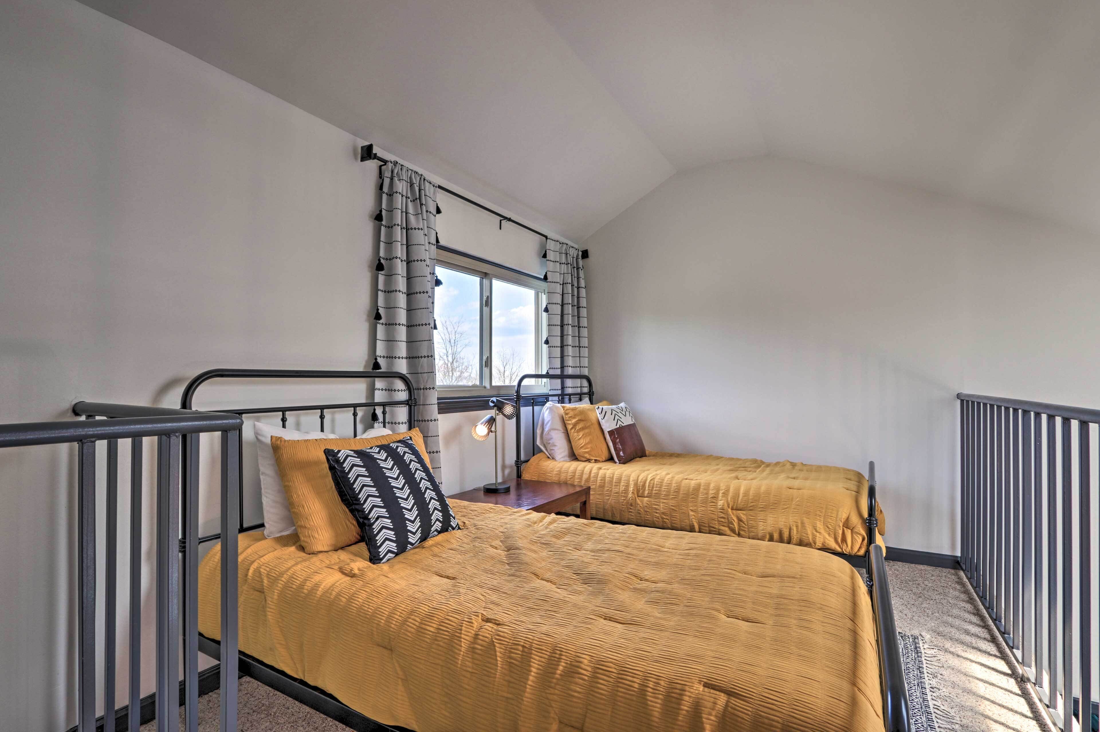 Una habitación con dos camas, una ventana con cortinas, una mesita pequeña y una barandilla.