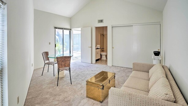 Uma sala de estar espaçosa com um sofá bege, uma mesa de centro de vidro e uma poltrona de vime. Um baú antigo está no chão.