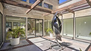 Um pátio moderno ao ar livre com uma escultura de metal, plantas em vasos e uma vista clara do interior através de grandes portas de vidro.