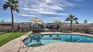 Ein Swimmingpool mit Liegestühlen und Sonnenschirmen, umgeben von Palmen und Häusern.