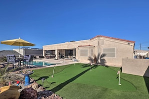 A house with a swimming pool, patio furniture, and a well-maintained lawn.