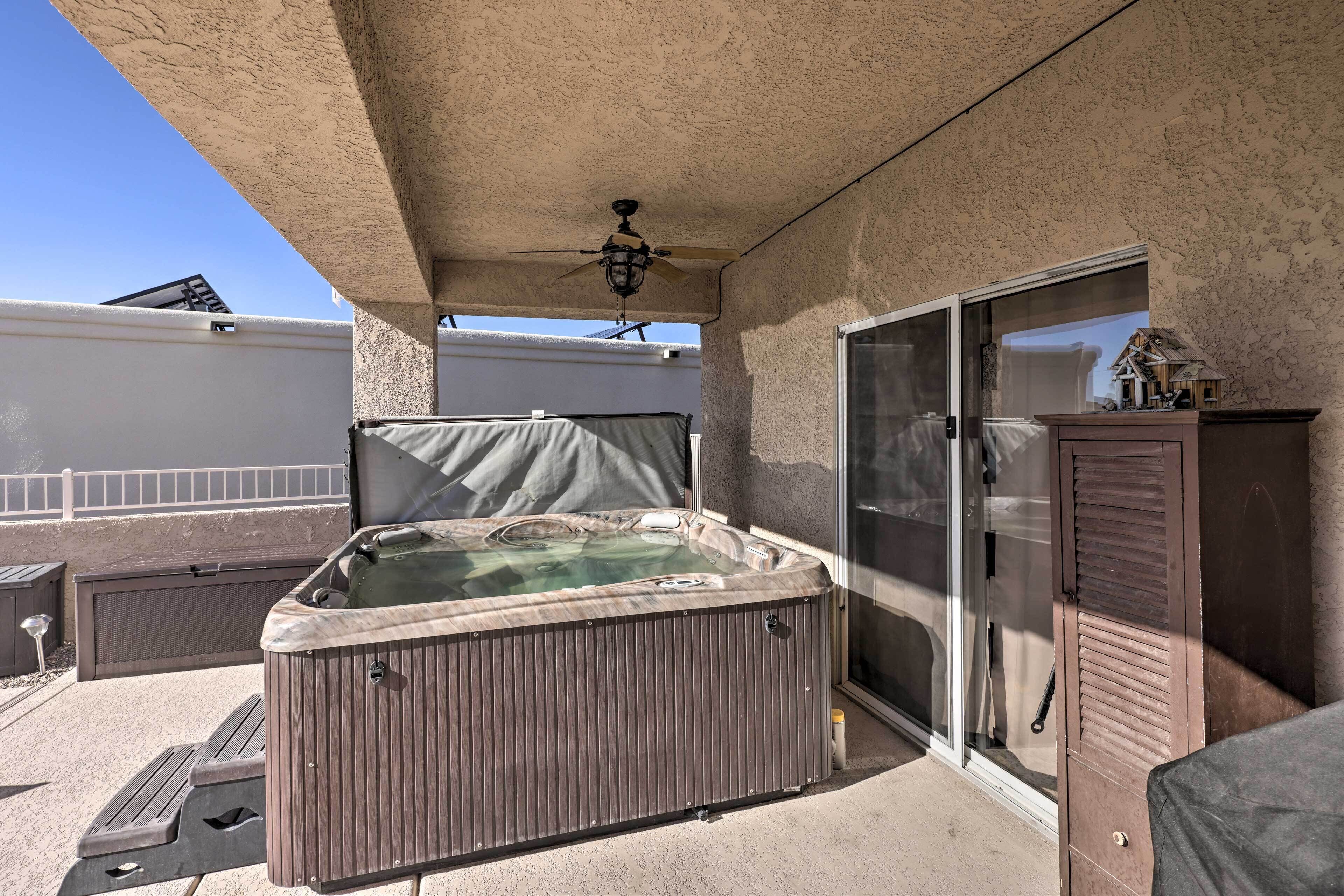 A hot tub under a covered patio area with a ceiling fan, a sliding glass door, and a small cabinet.