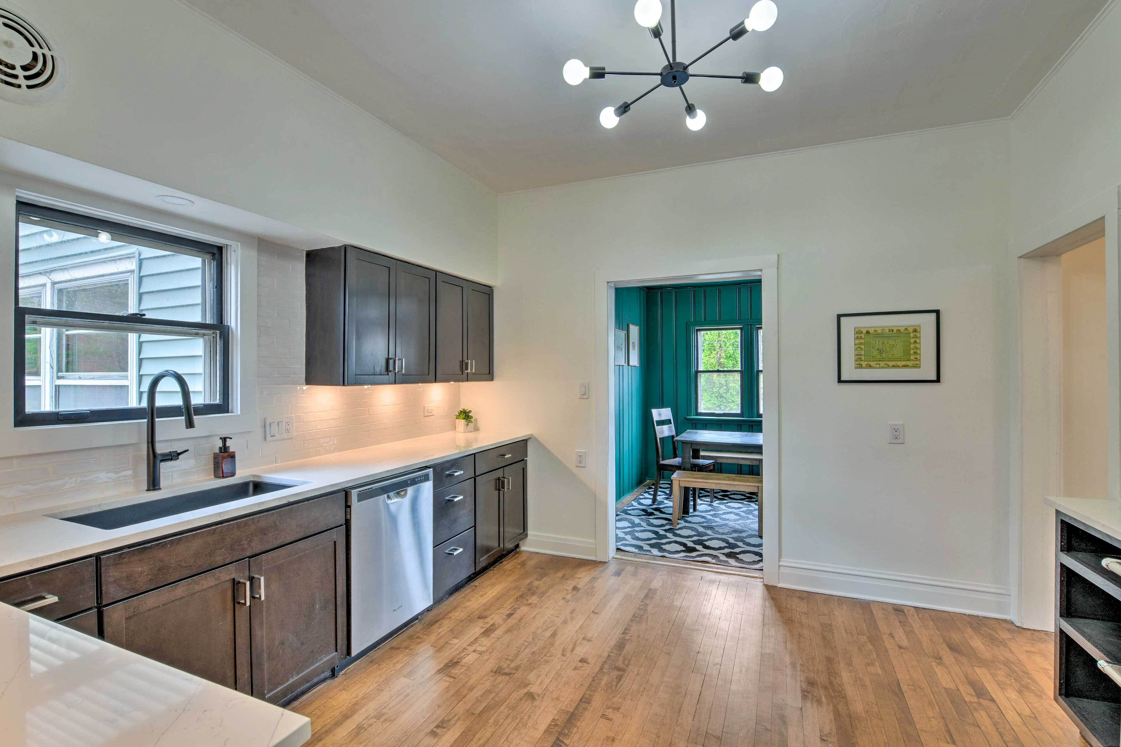 A modern kitchen with dark cabinets, a stainless steel dishwasher, and a window with blinds.