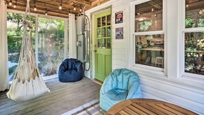 A cozy porch with a hanging macrame chair, a blue bean bag chair, and a wooden table. - Whimsical Bat Cave Cottage w/ Fire Pit! (Hendersonville)