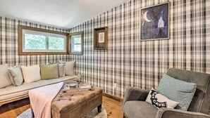 A cozy living room with a plaid-patterned wall, a sofa, a chair, and a coffee table. - Whimsical Bat Cave Cottage w/ Fire Pit! (Hendersonville)