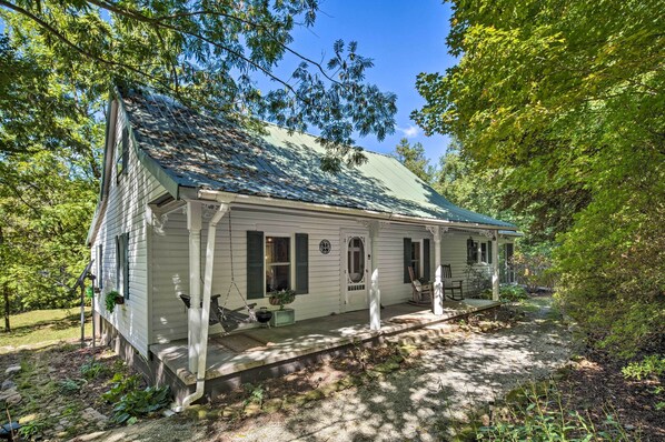 A single-story house with a green roof, a porch with a swing, and a small garden area.