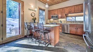 A kitchen with wooden cabinets, a stainless steel refrigerator, and a large island with bar stools. - Shuttle to Ski Resort: Northstar Home! (Truckee)