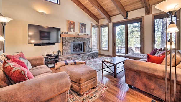A spacious living room with a stone fireplace, wooden ceiling beams, and large windows offering a view of the outdoors. - Shuttle to Ski Resort: Northstar Home! (Truckee)