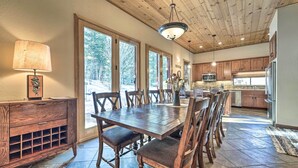 A spacious dining area with a wooden table and chairs, a wooden cabinet with drawers, and a large window with a view of trees. - Shuttle to Ski Resort: Northstar Home! (Truckee)