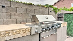 Cozinha externa com churrasqueira embutida, painel de azulejos e parede de pedra.