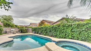 Piscina com design curvo, rodeada por um terraço de pedra e um sebe.