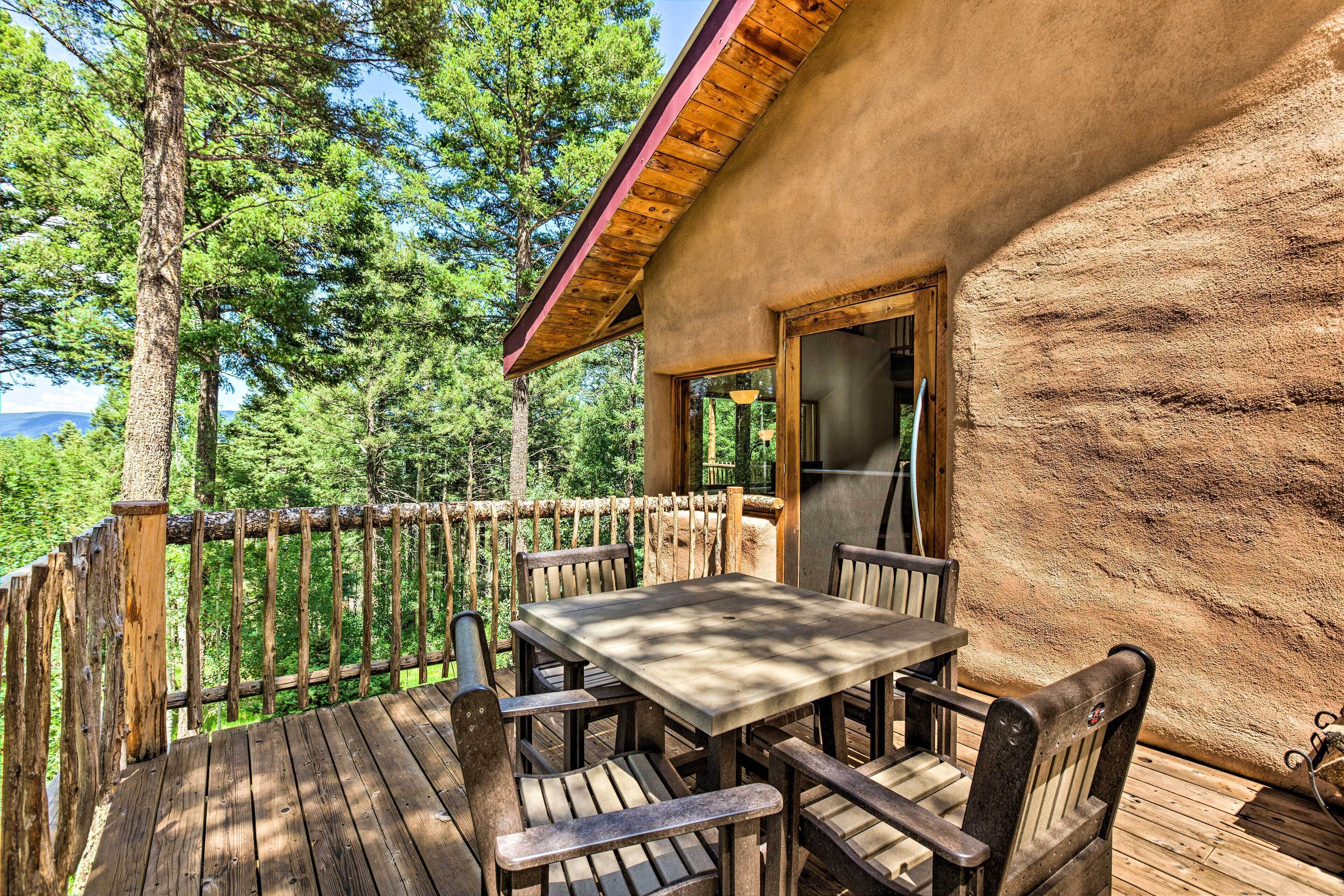 A wooden deck with a table and chairs, surrounded by a wooden railing, overlooking a forested area.