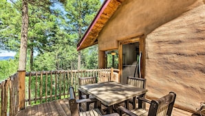 A wooden deck with a table and chairs, surrounded by a wooden railing, overlooking a forested area. - Angel Fire Cabin w/ Deck ~ 2 Mi to Ski & Hiking! (Angel Fire)