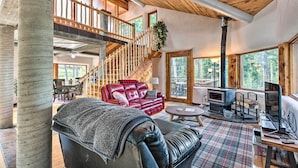 A spacious living area with a red leather sofa, a black leather couch, and a wooden staircase. - Angel Fire Cabin w/ Deck ~ 2 Mi to Ski & Hiking! (Angel Fire)