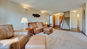 Un salon avec un canapé en cuir marron, un pouf assorti, une lampe et un luminaire fixé au mur.