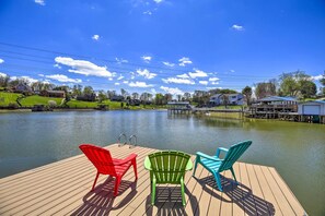 A wooden dock with three Adirondack chairs facing a calm lake, surrounded by houses and a clear blue sky. - Lake House Haven: Fire Pit, Boat Dock + More! (Johnson City)