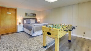 A bedroom with a bed, a bedside table with a lamp, a wooden foosball table, and a private door. - Lake House Haven: Fire Pit, Boat Dock + More! (Johnson City)