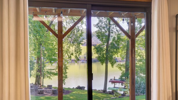 A view through a glass door to a patio area with a fire pit, outdoor seating, and a lake. - Lake House Haven: Fire Pit, Boat Dock + More! (Johnson City)