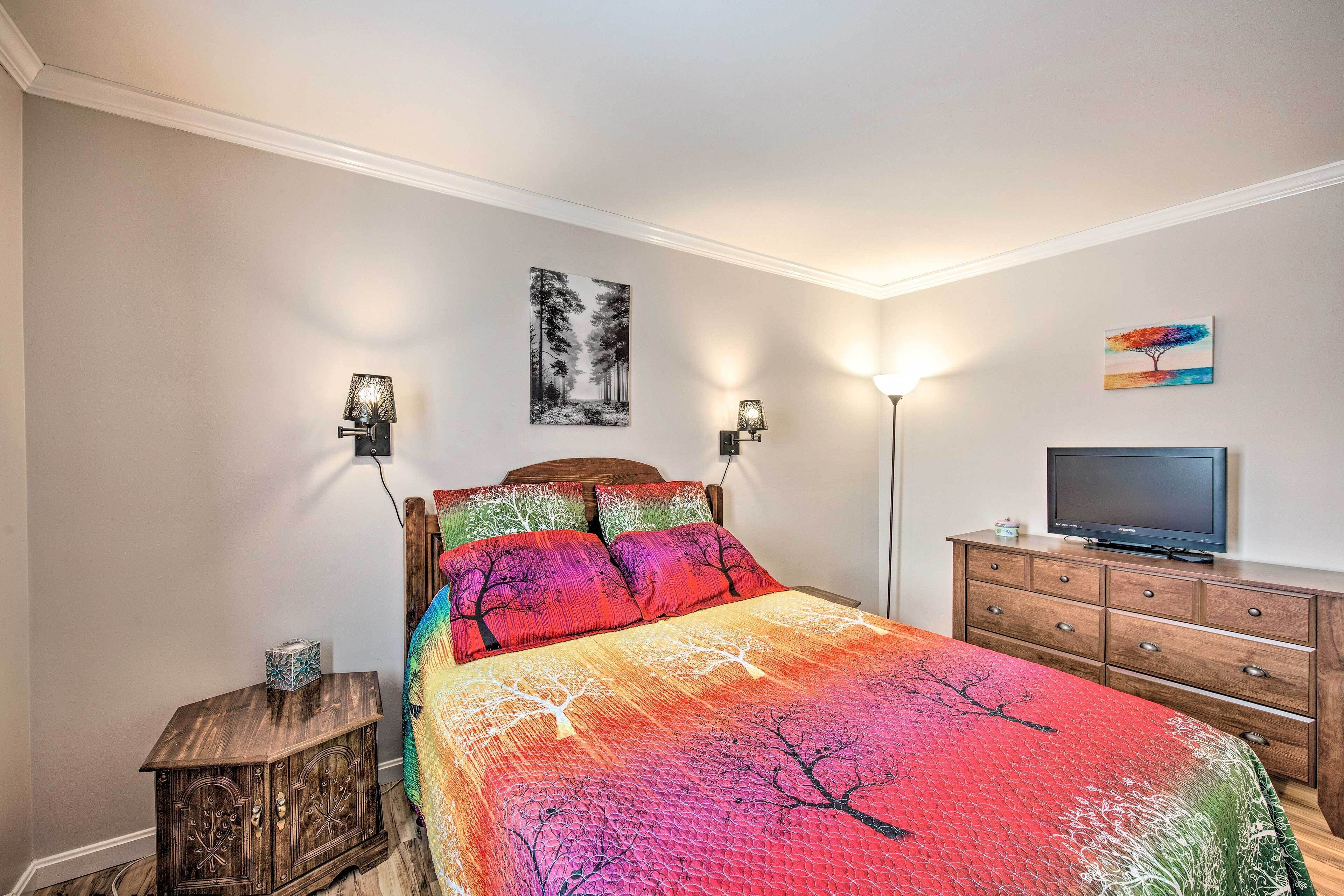 Un dormitorio con cama, cómoda, televisor y lámparas de pared.