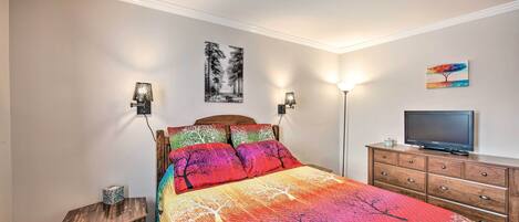 Un dormitorio con cama, cómoda, televisor y lámparas de pared.